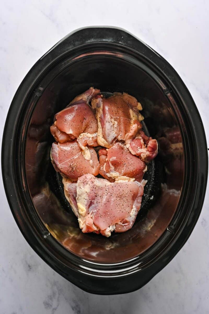 Uncooked chicken pieces added to a crockpot.