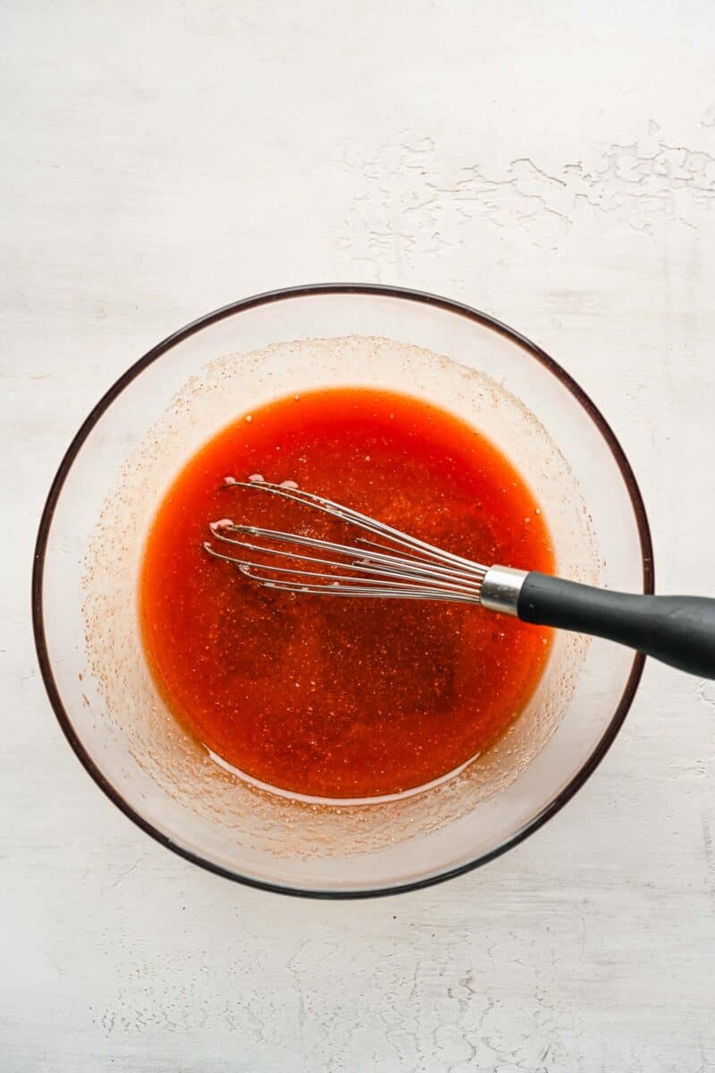 Sweet and sour sauce in a glass bowl with a whisk.
