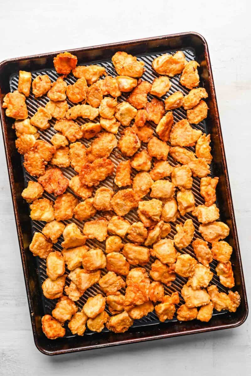 Pan-fried chicken pieces spread out on a baking sheet.