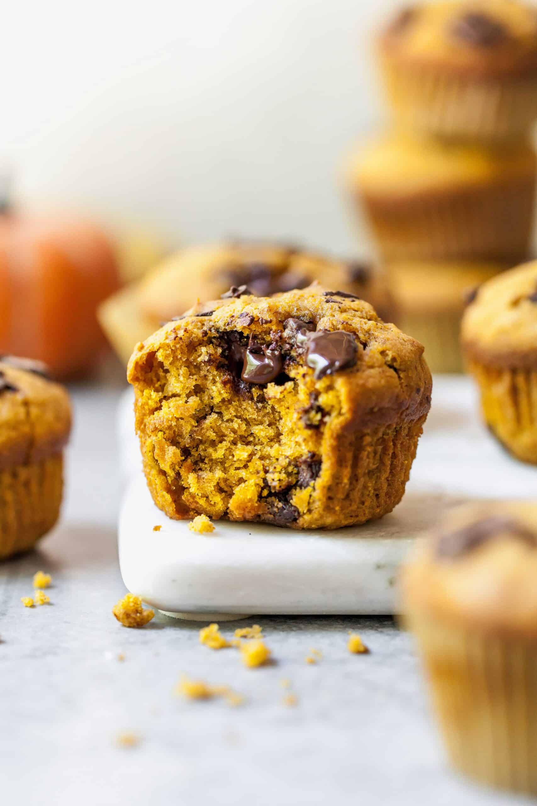 Closeup of a pumpkin chocolate chunk muffin with a bite missing on a marble countertop.