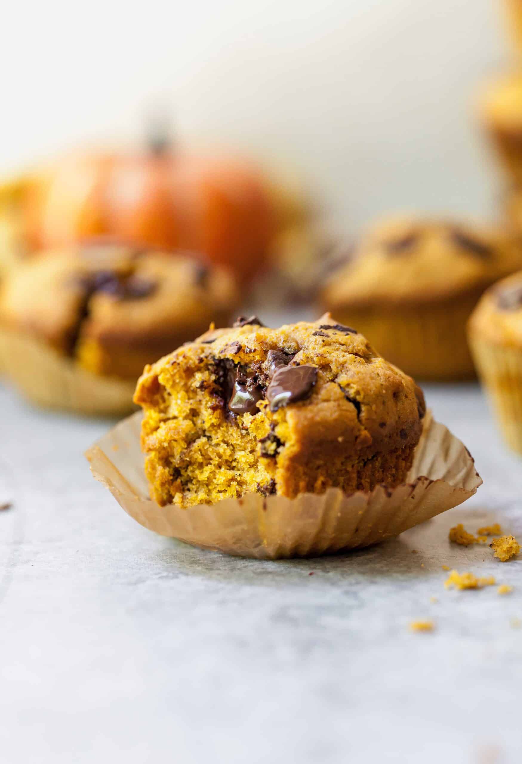 Closeup of a pumpkin chocolate chunk muffin with a bite missing on a marble countertop.