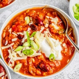 Close up of a bowl of turkey pumpkin chili, topped with cheese, green onions, and sour cream