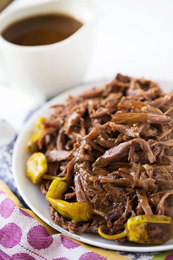 Mississippi roast on a white plate with pepperoncini on the bottom. The plate is sitting on top of a purple polka dotted towel with a gravy boat in the background.