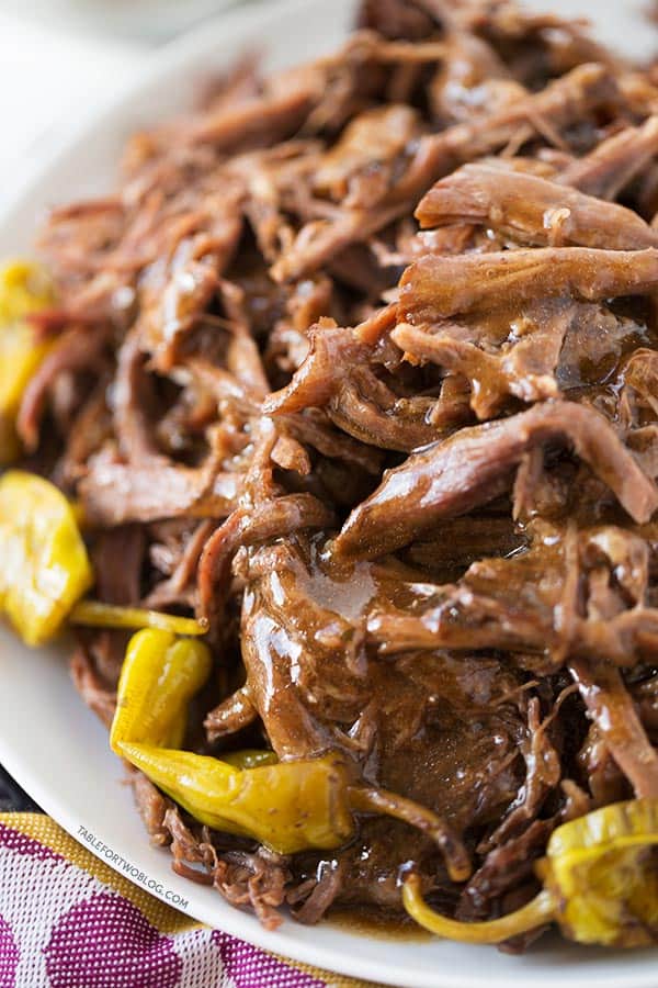 Up close shot of Mississippi roast with the au jus smothered on top. Pepperoncini can be seen along the rim of the white plate that the roast is plated on.