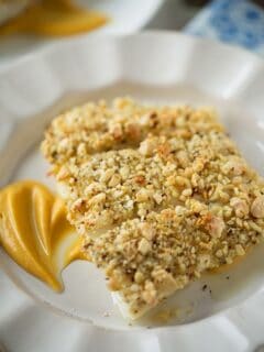 Three baked almond-crusted halibut fillets on a plate over a bed of sweet potato puree.