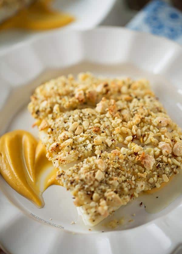 Three baked almond-crusted halibut fillets on a plate over a bed of sweet potato puree.