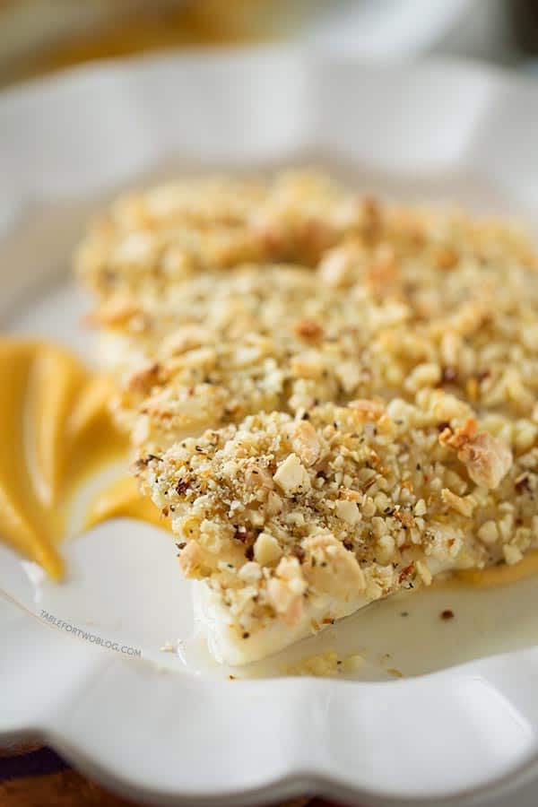 Three baked almond-crusted halibut fillets on a plate over a bed of sweet potato puree.