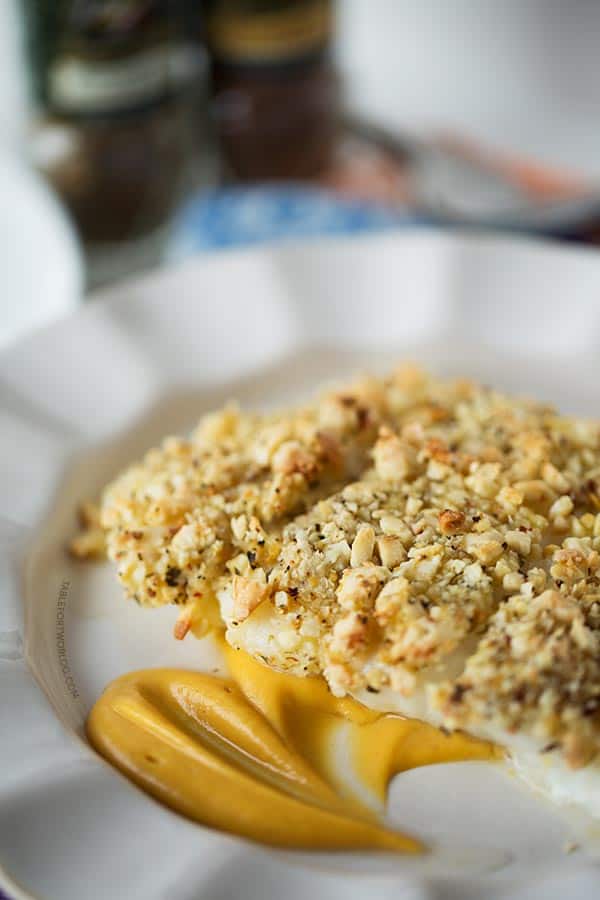 Three baked almond-crusted halibut fillets on a plate over a bed of sweet potato puree.