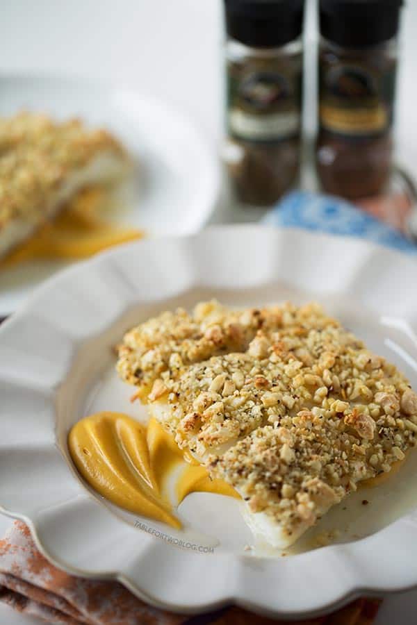 Three baked almond-crusted halibut fillets on a plate over a bed of sweet potato puree.