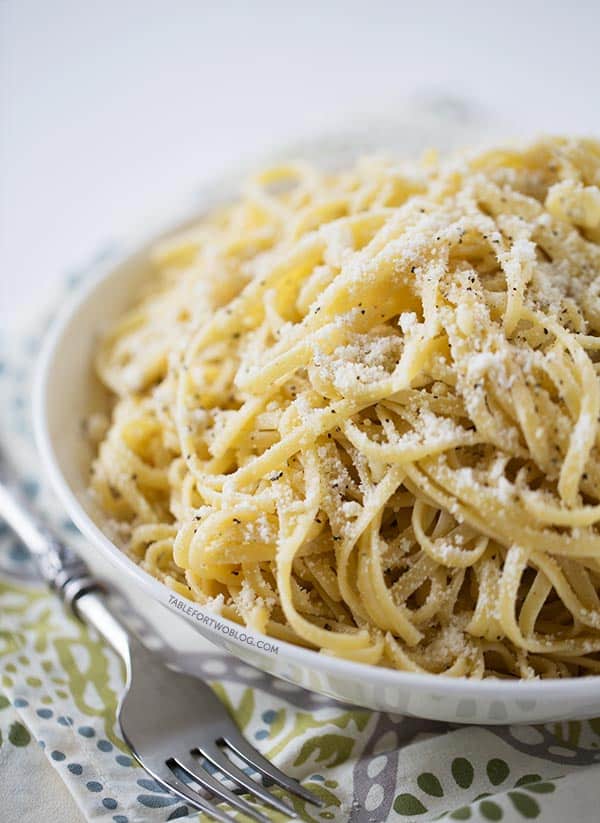 Cacio e pepe is a traditional Italian pasta dish made with parmesan cheese and black pepper. It's rich, creamy, spicy, and easy to make. A bowl filled with cacio e pepe, topped with parmesan cheese nad black pepper, next to a fork, on top of a placemat.