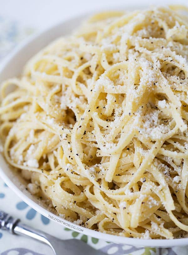 A bowl of cacio e pepe topped with parmesan cheese and black pepper, next to a fork.