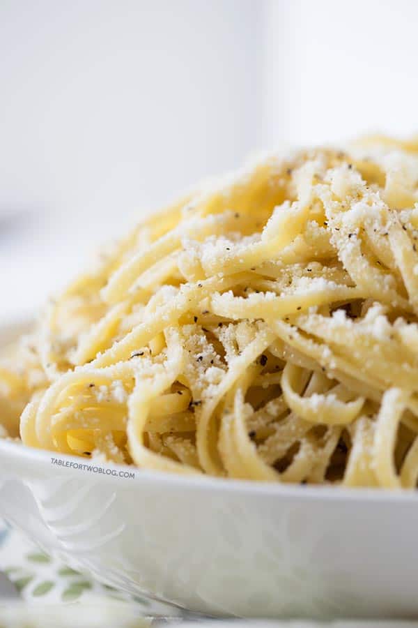 Close up of a bowl of cacio e pepe, topped with parmesan cheese and black pepper. 