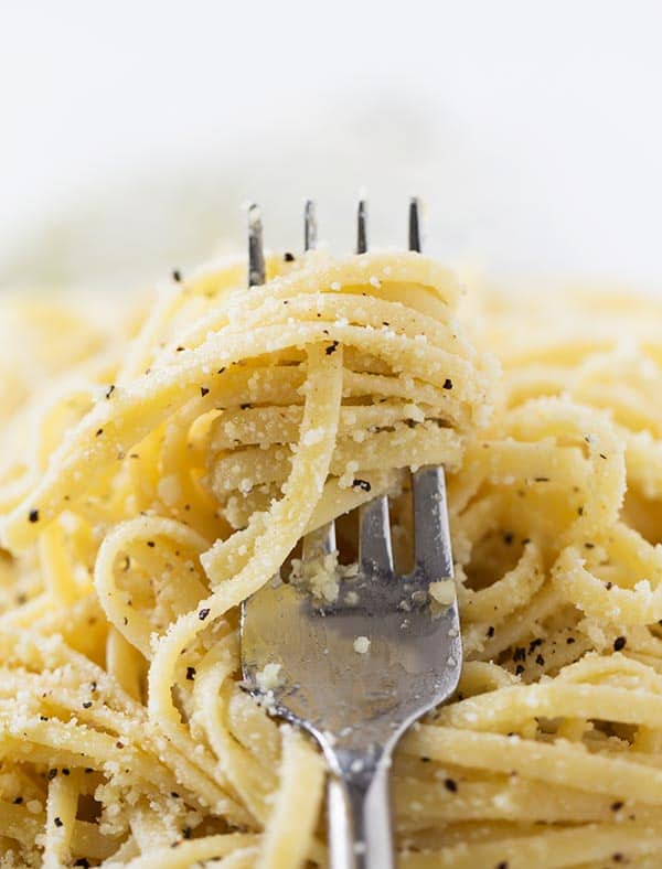 Close up of a fork wrapped with cacio e pepe spaghetti, covered in ground pepper and parmesan cheese.