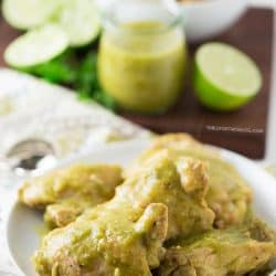 Slow cooker salsa verde chicken on a plate next to salsa verde, limes, and a bowl of quinoa.