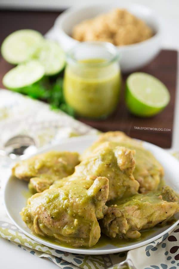 Slow cooker salsa verde chicken on a plate next to salsa verde, limes, and a bowl of quinoa.