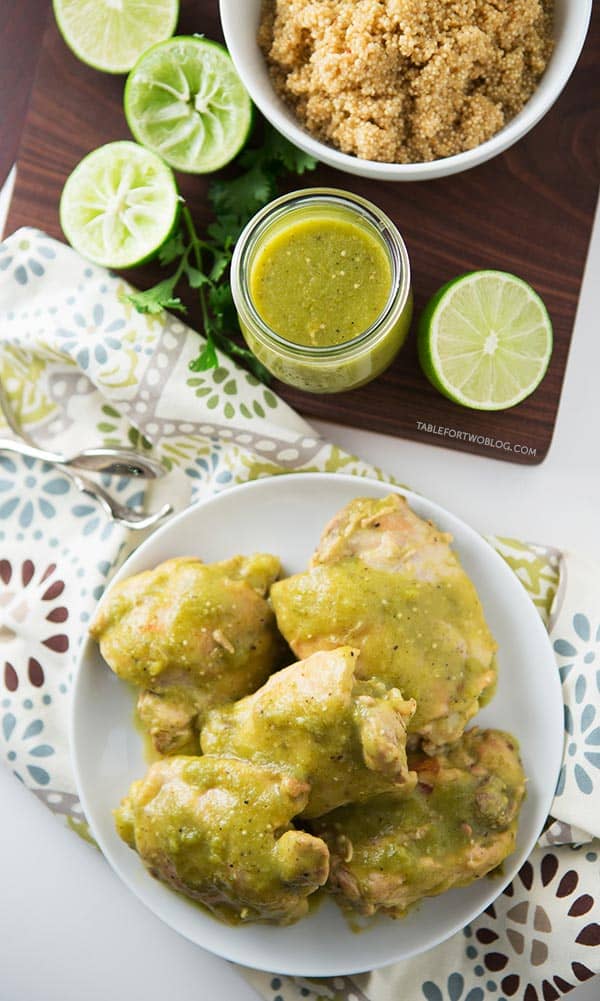 Slow cooker salsa verde chicken on a plate next to salsa verde, limes, and a bowl of quinoa.