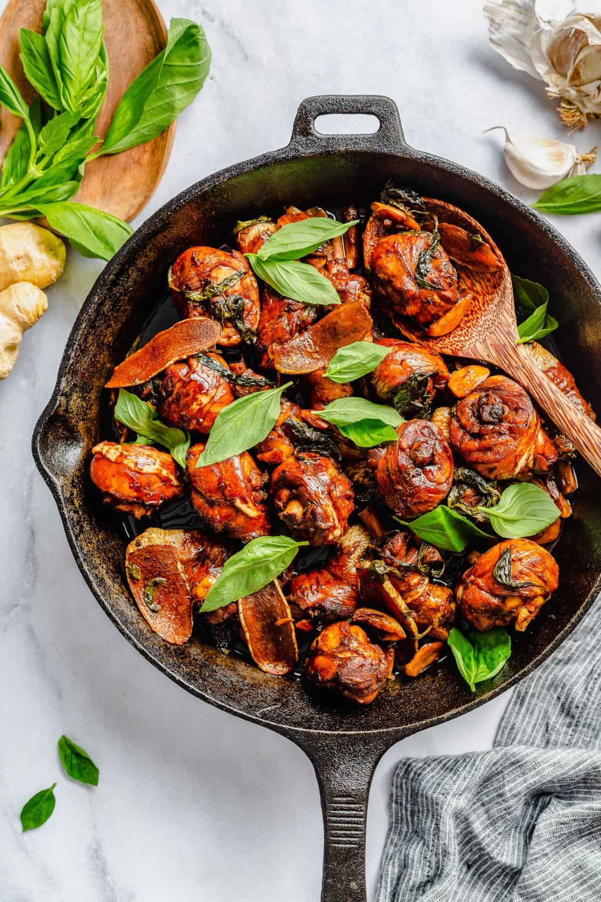 Three cup chicken in cast iron skillet with basil leaves.