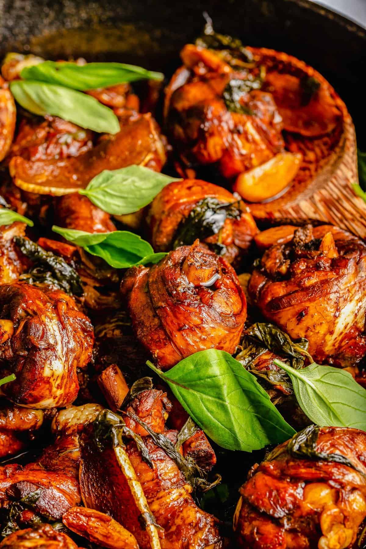 Closeup of three cup chicken in skillet with basil leaves.