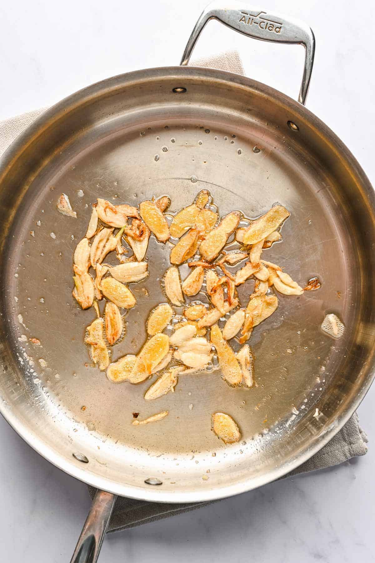 Overhead view of smashed garlic cloves sauteing in a metal skillet.