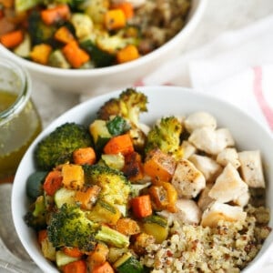 Two quinoa bowls topped with roasted vegetables and chicken.