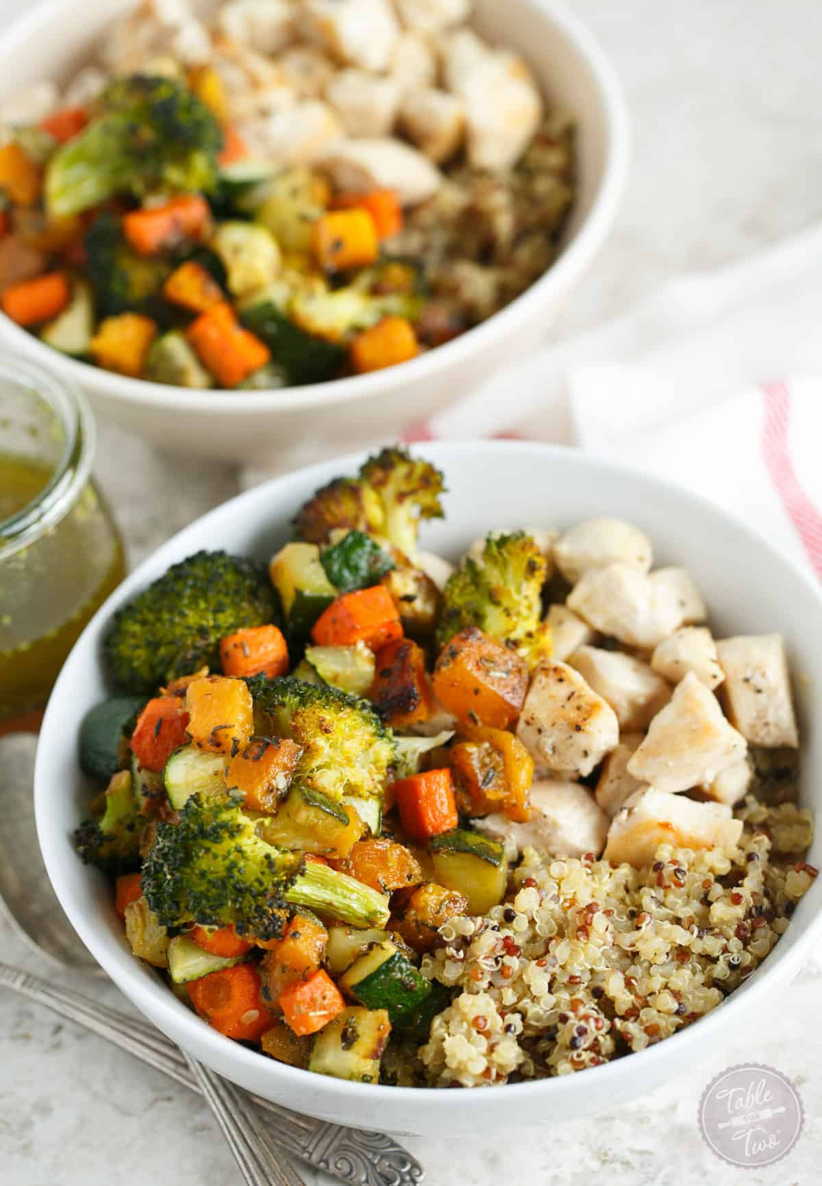 Two quinoa bowls topped with roasted vegetables and chicken.