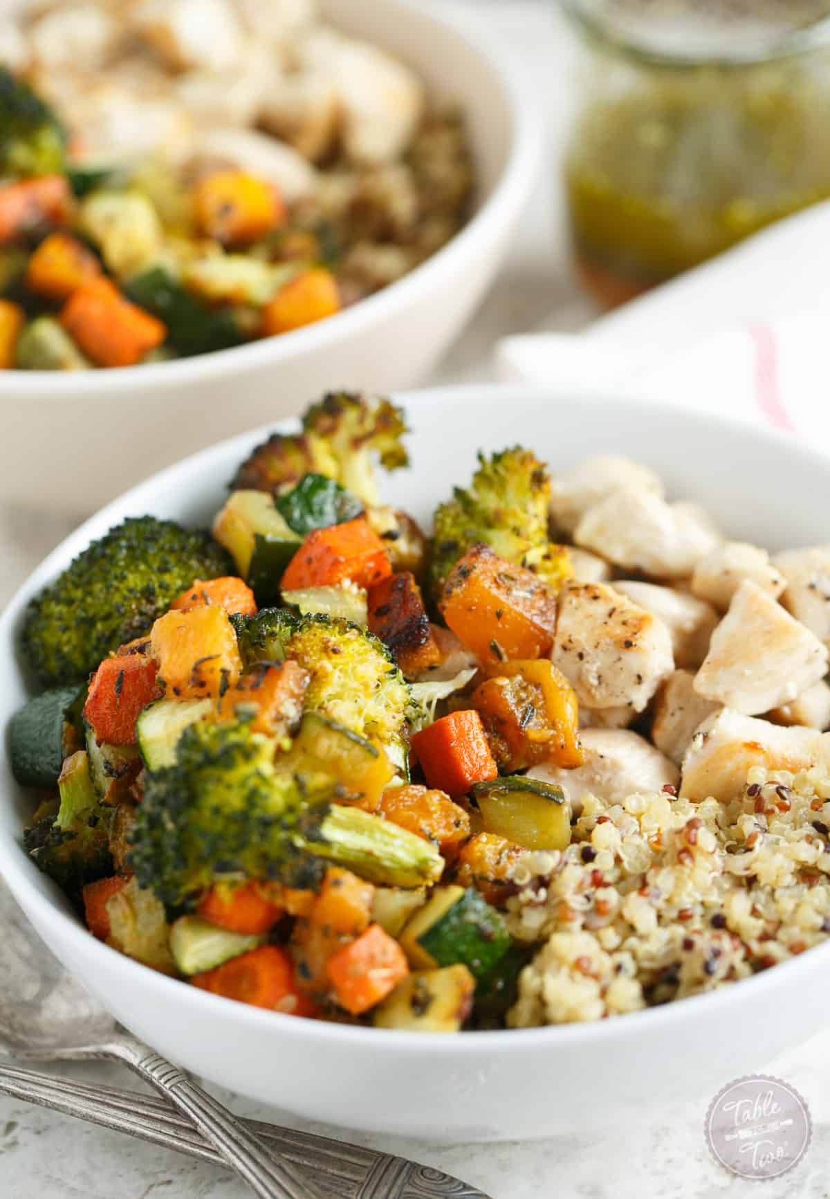 Two quinoa bowls topped with roasted vegetables and chicken.