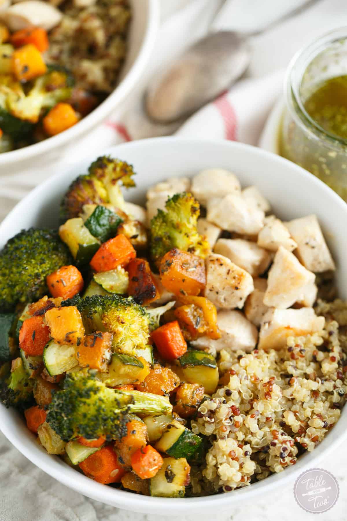 Two quinoa bowls topped with roasted vegetables and chicken.