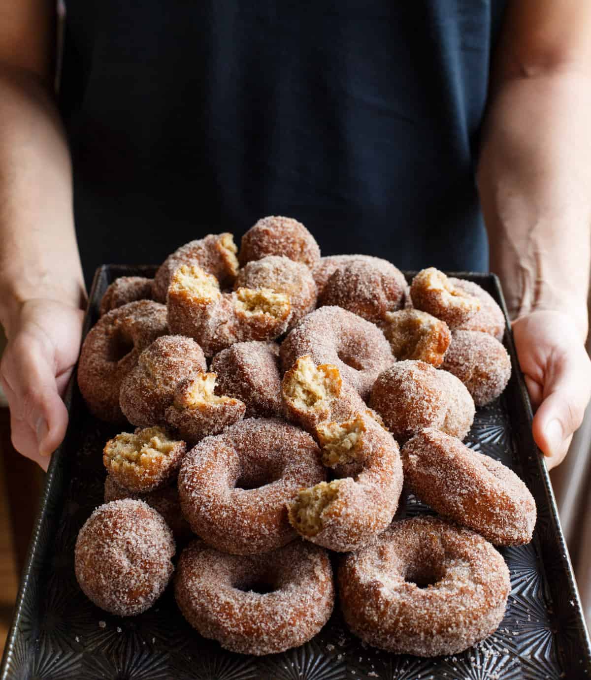 Person holding baking sheet full of homemade apple cider doughnuts