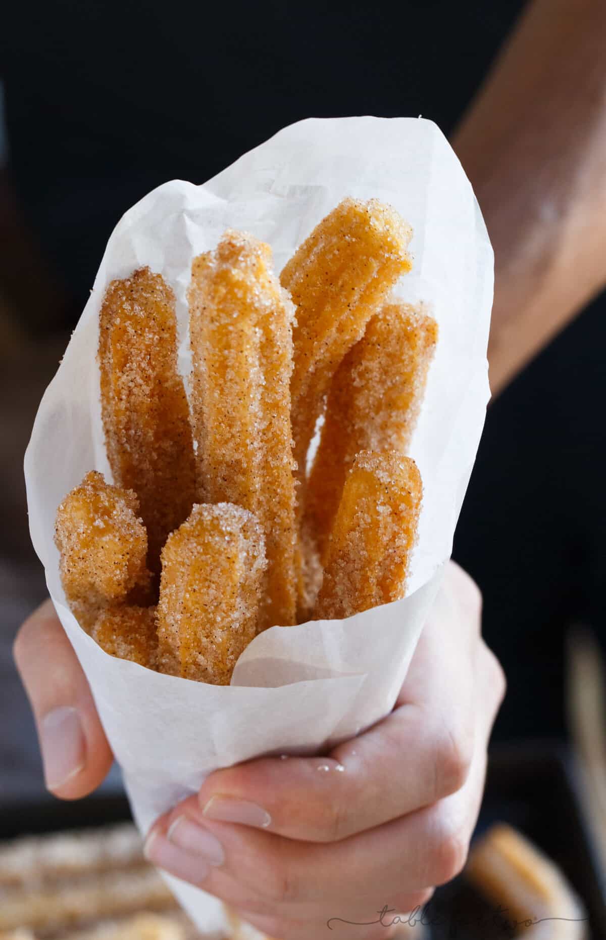 Mexican churros wrapped in paper and held in a hand.