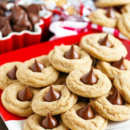 Peanut butter blossom cookies on Christmas plates near unwrapped chocolate kisses.