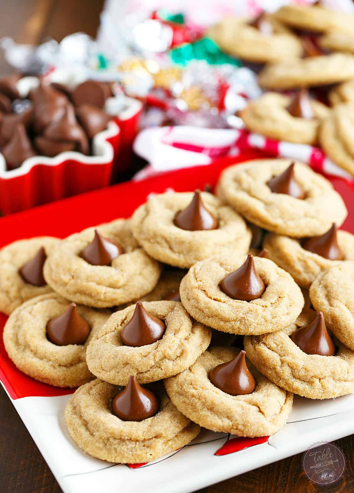 Peanut butter blossom cookies on Christmas plates near unwrapped chocolate kisses.