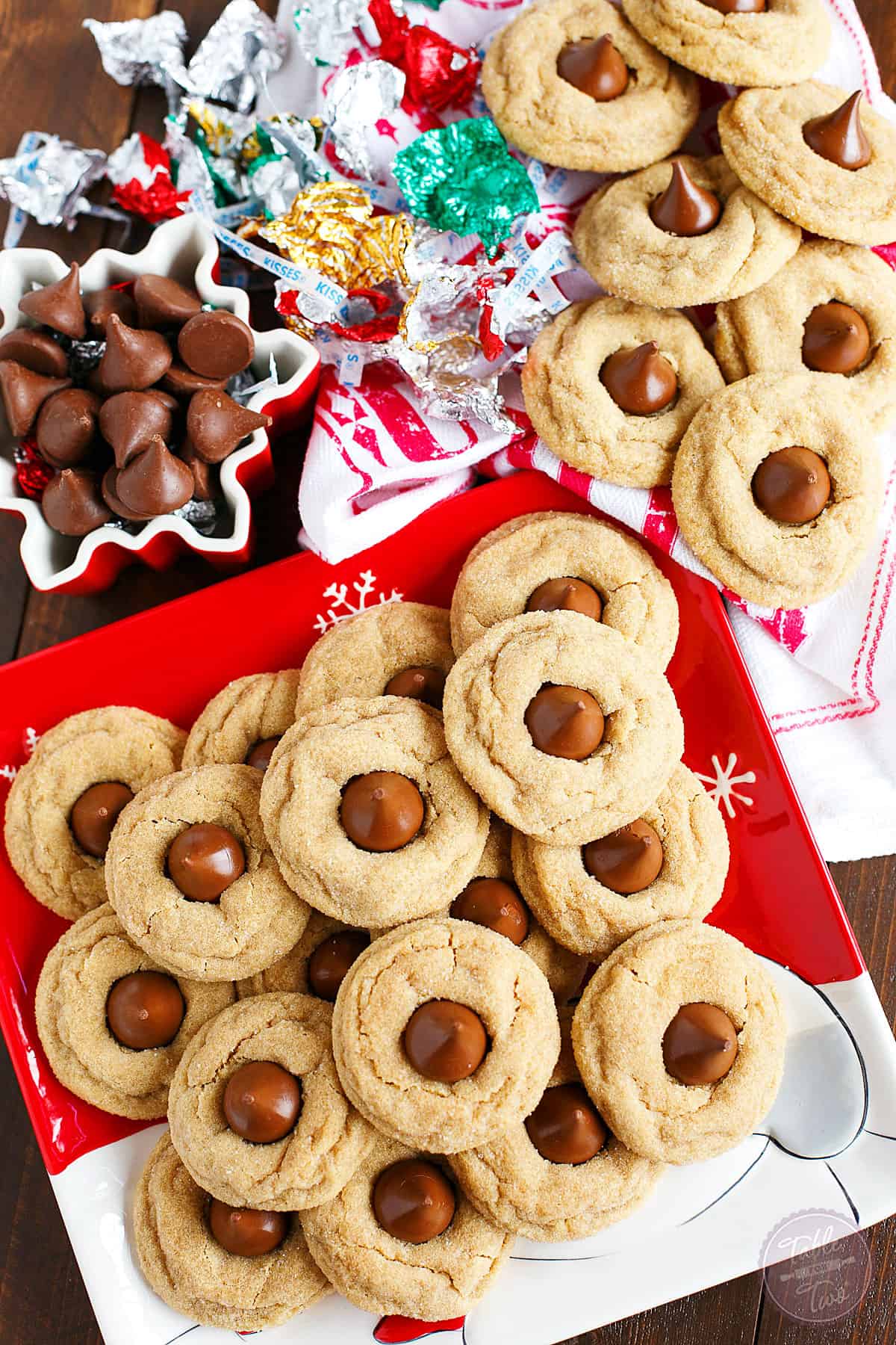 Peanut butter blossom cookies on a Christmas plate near unwrapped chocolate kisses.