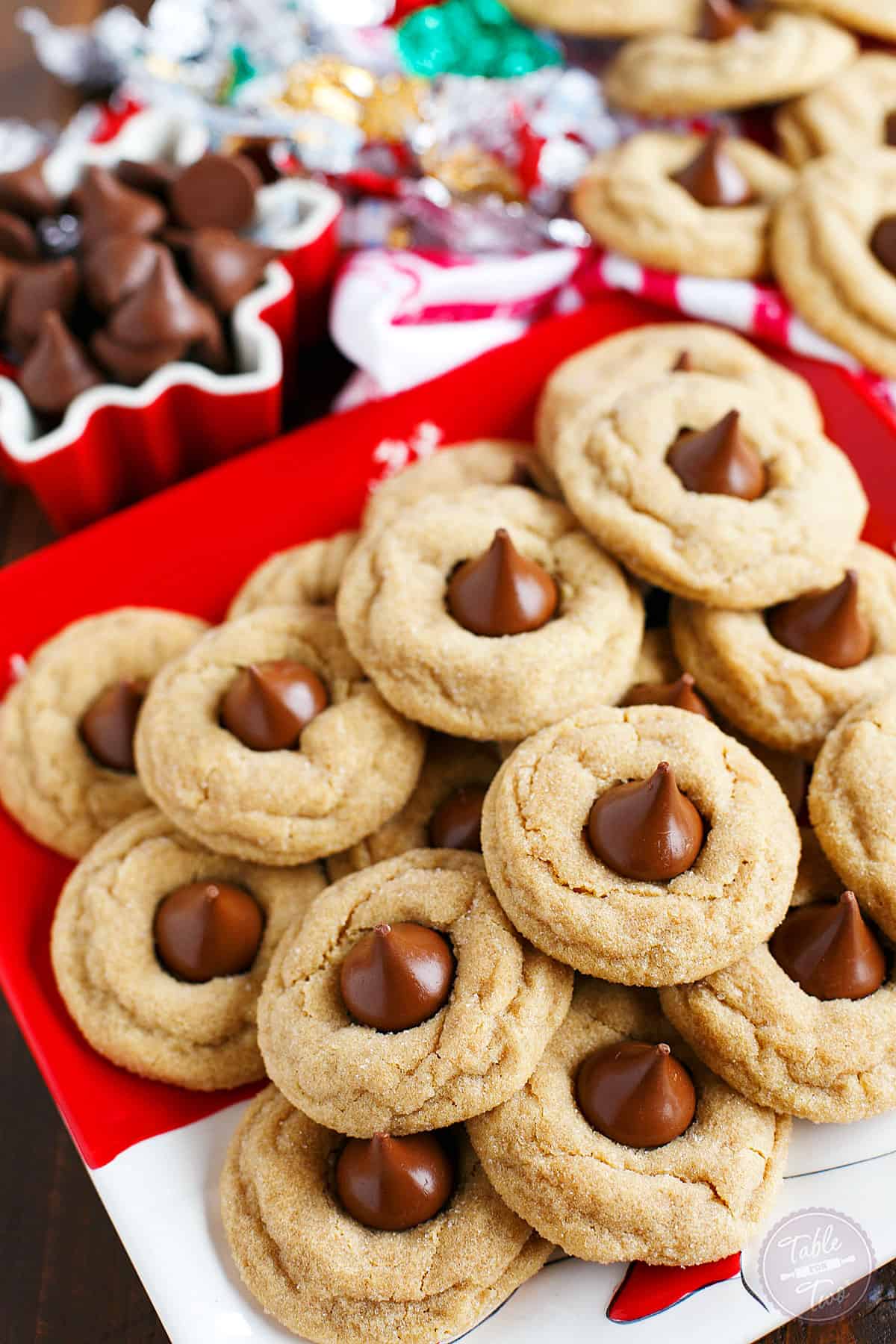 Peanut butter blossom cookies on a Christmas plate near unwrapped chocolate kisses.