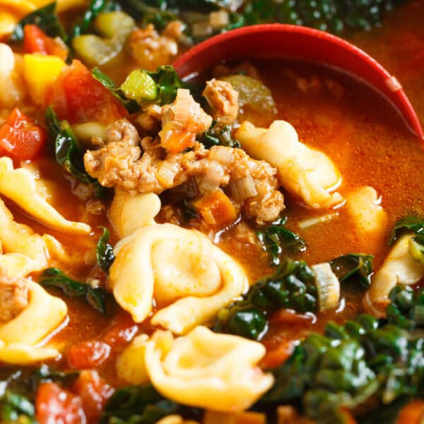 A ladle dips into a large pot of spicy sausage tortellini soup.