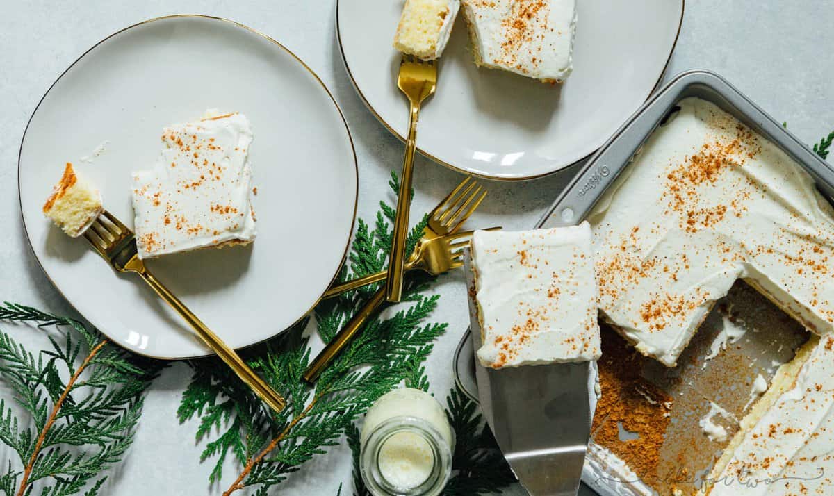 Overhead image of eggnog tres leches cake served out of the baking pan onto white gold rimmed plates with gold forks.