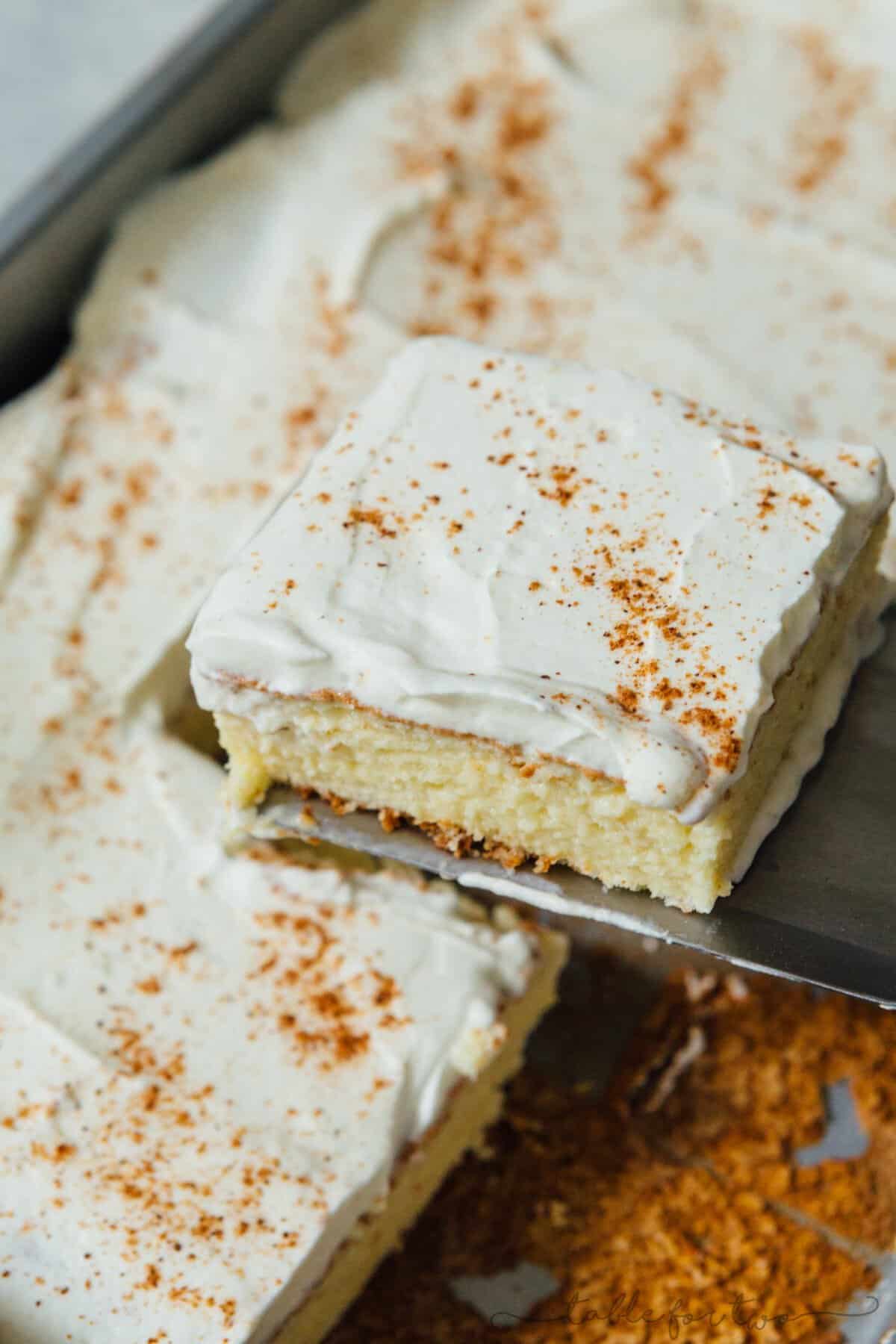 A slice of eggnog tres leches cake being lifted out of the baking pan with a metal serving spatula.