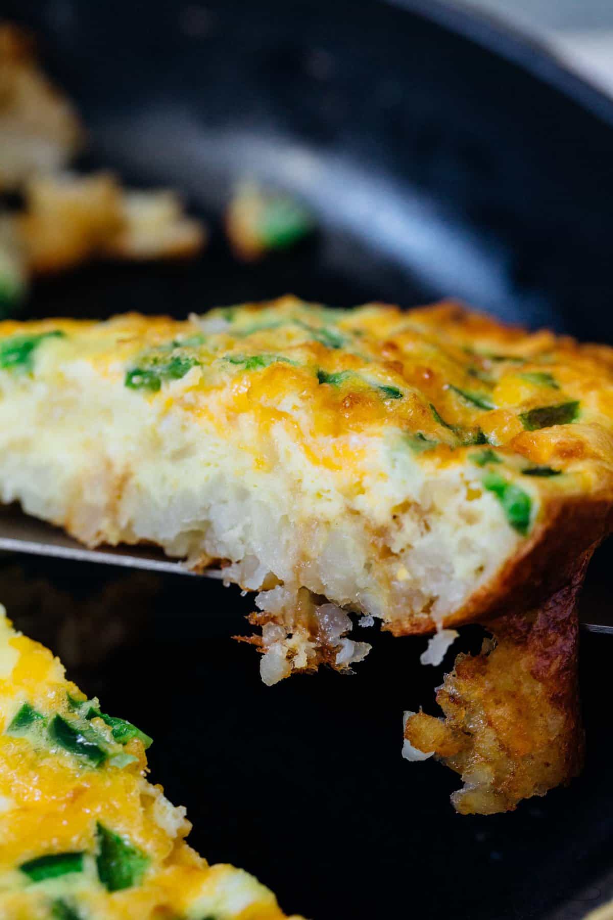 A slice of frittata lifted from a cast iron skillet.