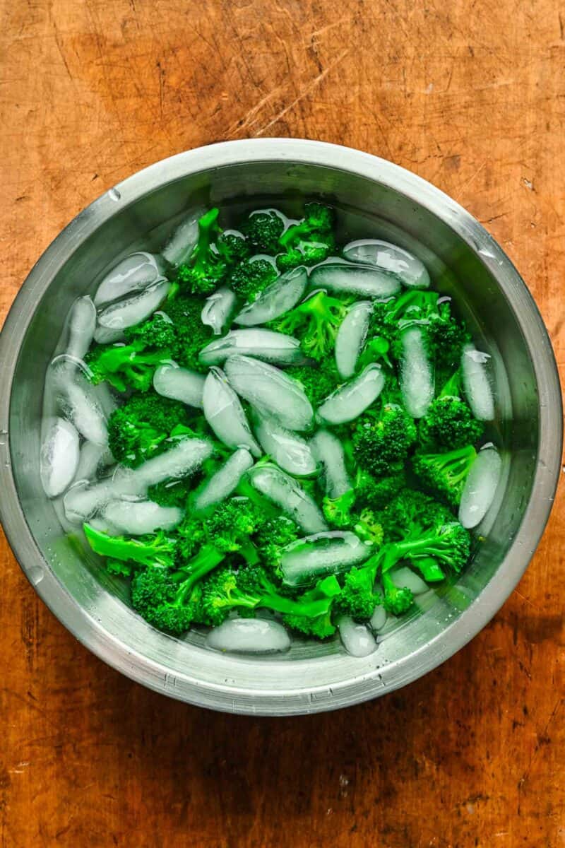 Blanched broccoli florets in a bowl of ice water.