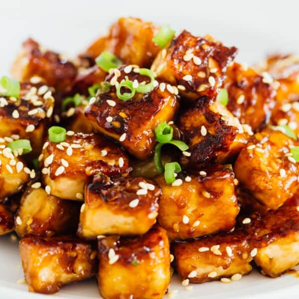 A pile of sesame garlic fried tofu on a plate garnished with sesame seeds.