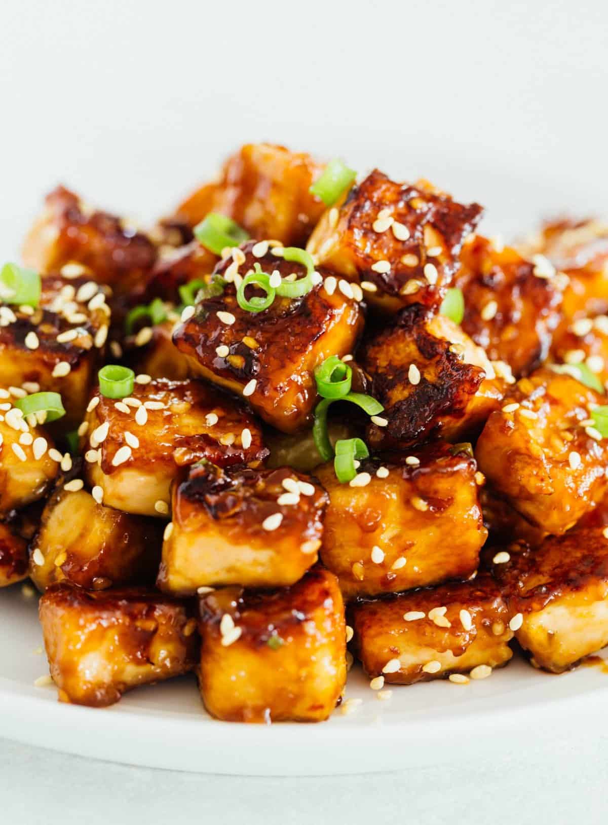A pile of sesame garlic fried tofu on a plate garnished with sesame seeds.