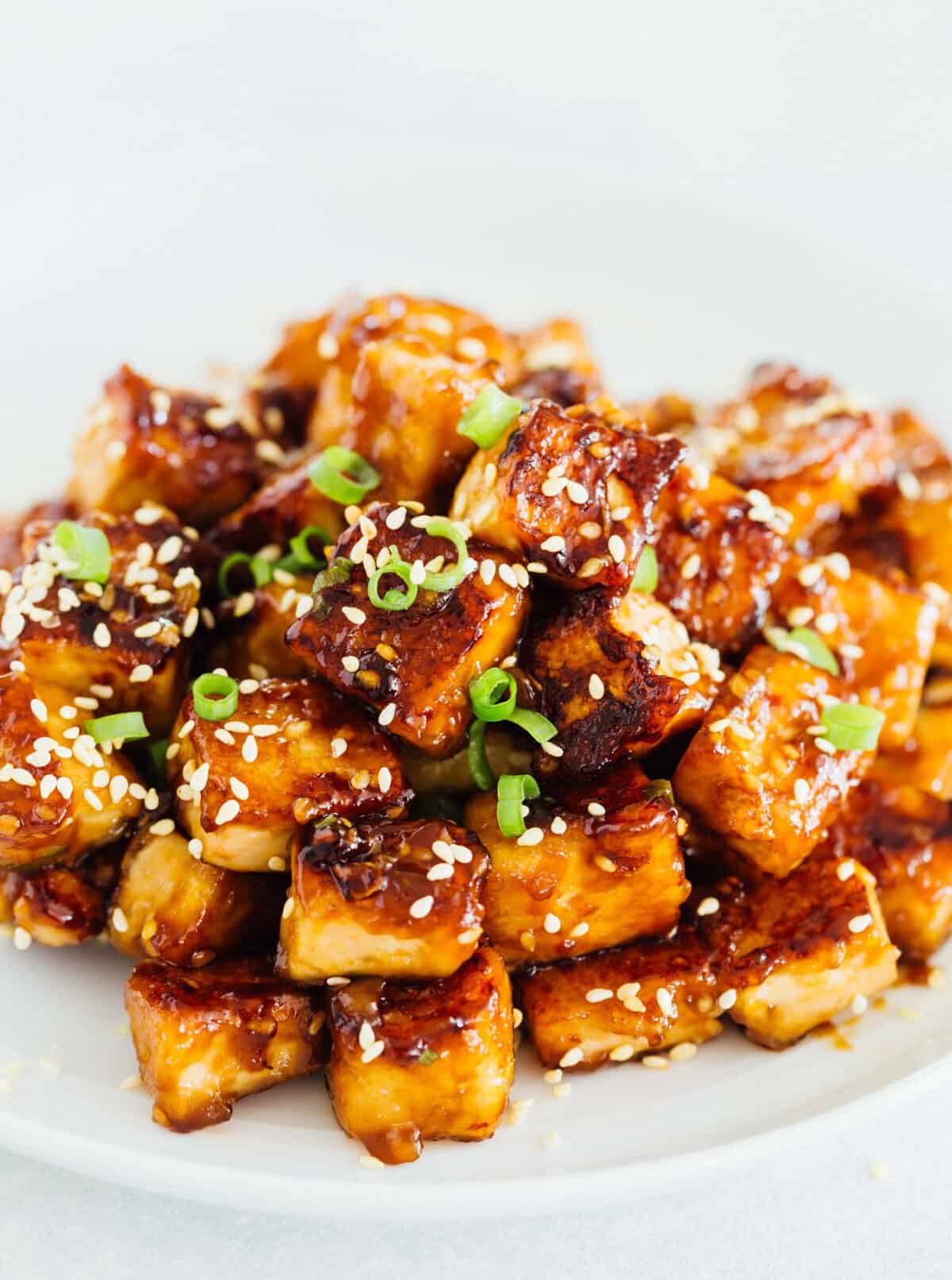 A pile of sesame garlic fried tofu on a plate garnished with sesame seeds.