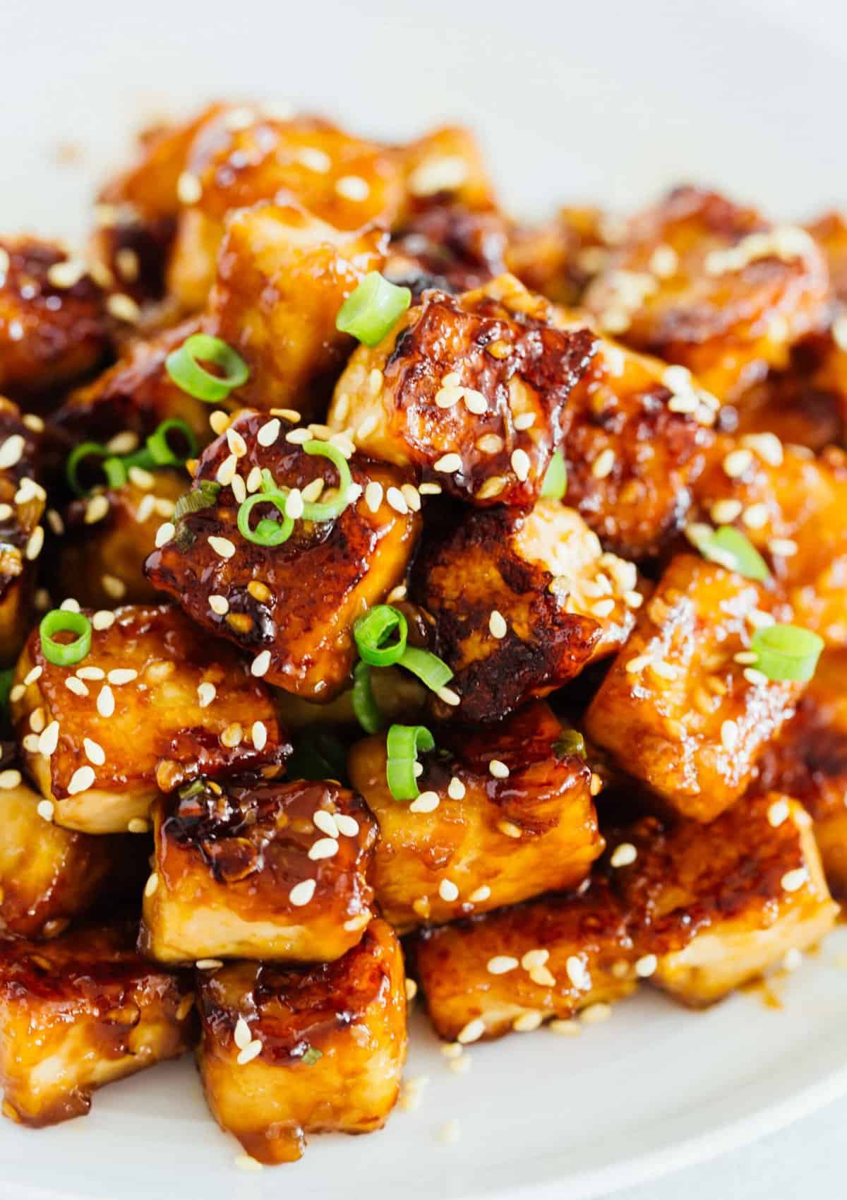 A pile of sesame garlic fried tofu on a plate garnished with sesame seeds.