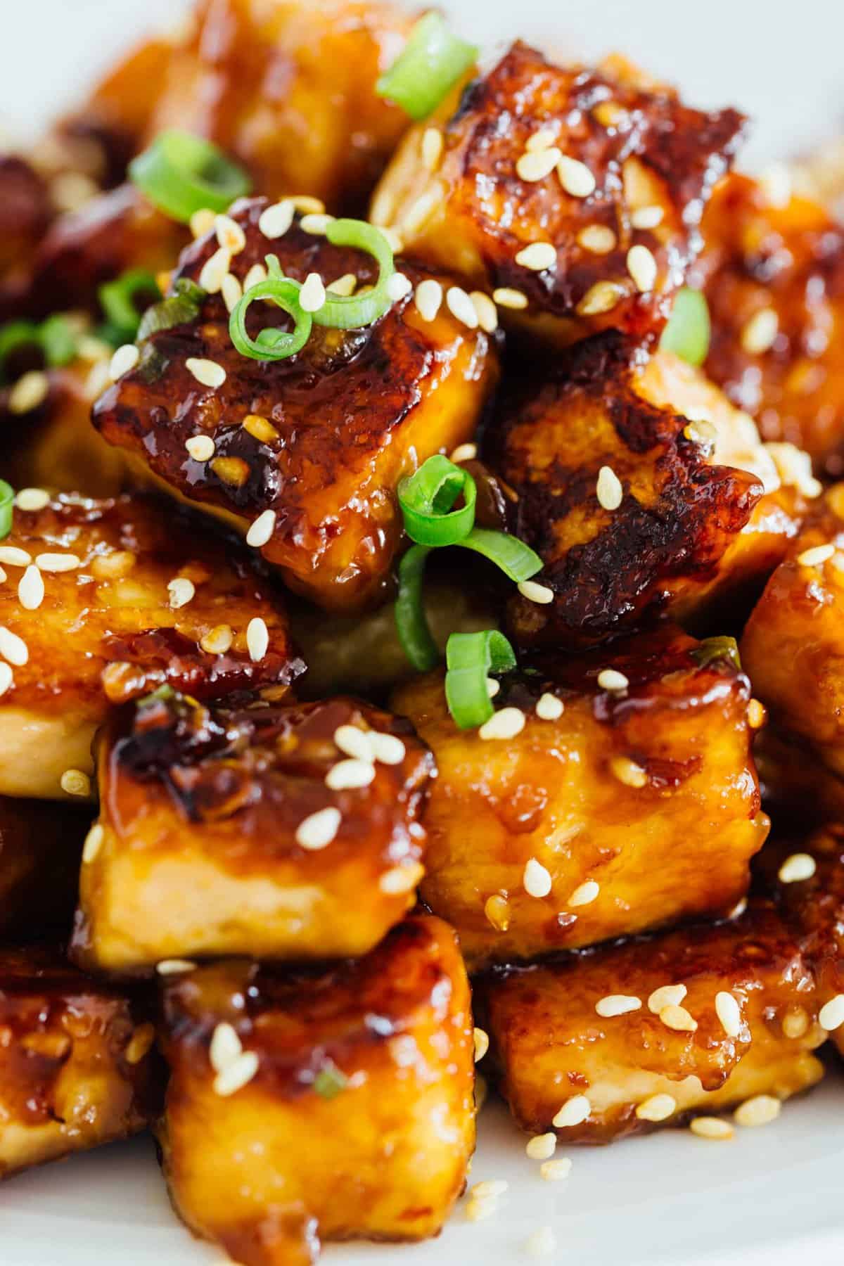 A pile of sesame garlic fried tofu on a plate garnished with sesame seeds.