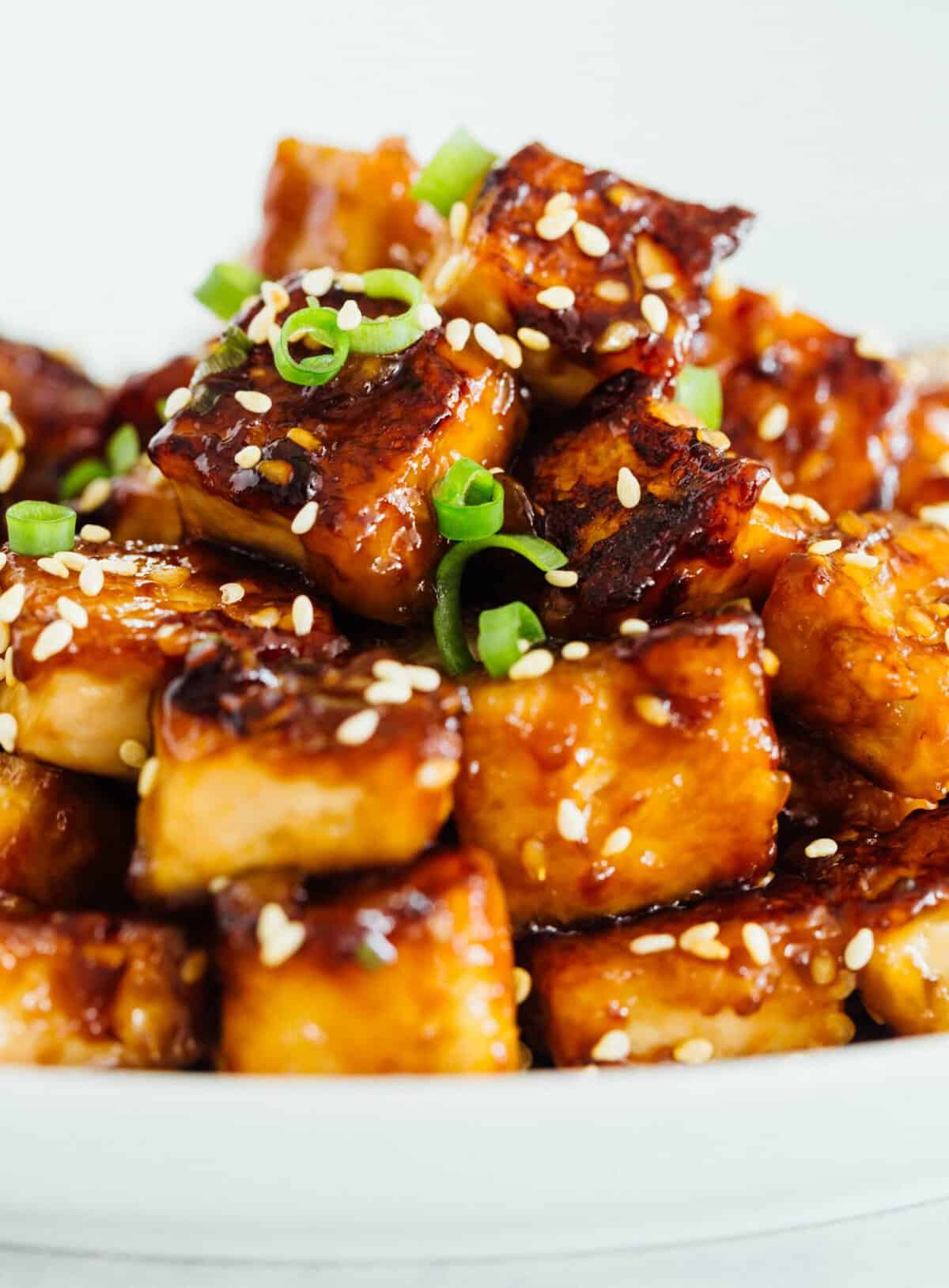 A pile of sesame garlic fried tofu on a plate garnished with sesame seeds.