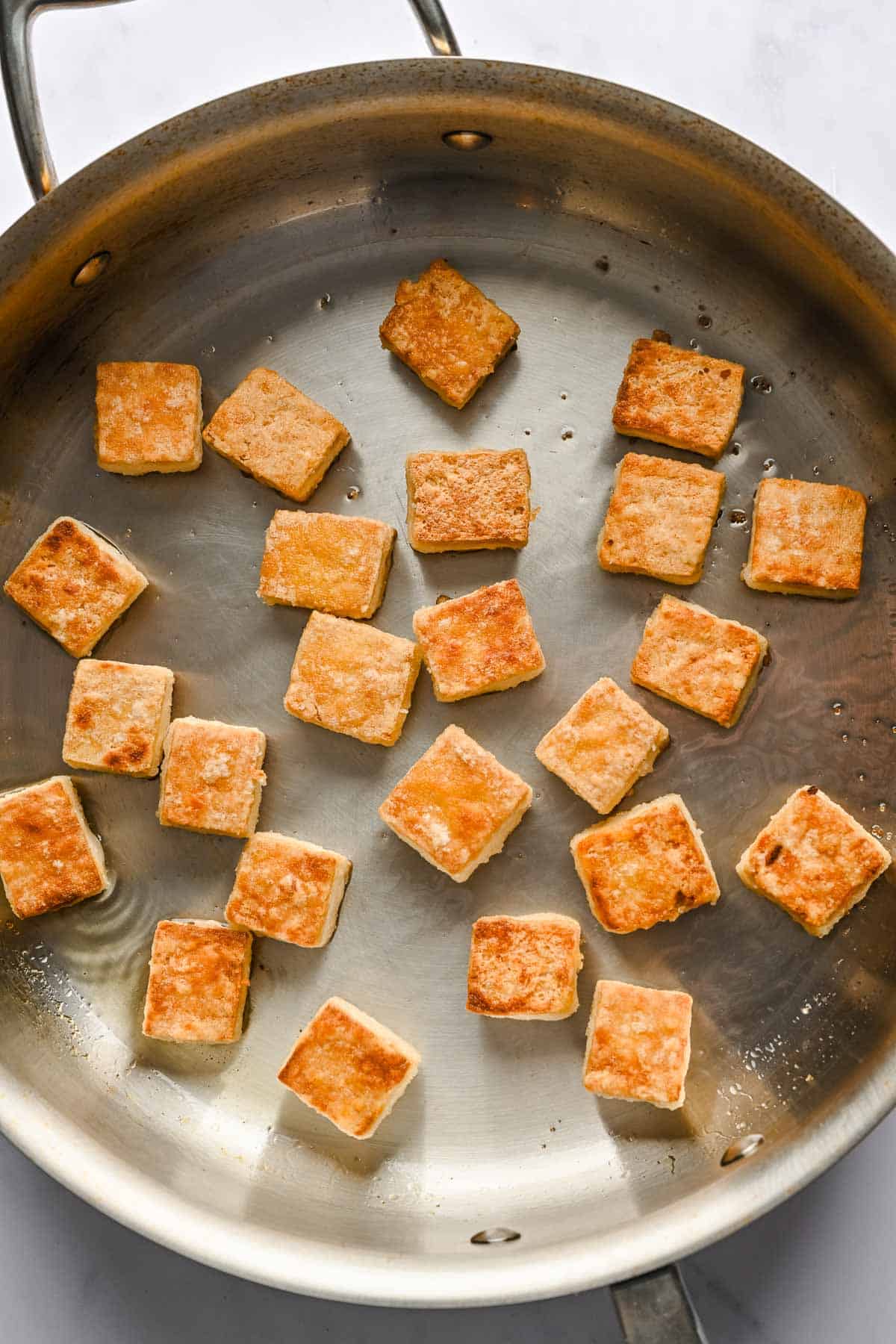 Tofu cubes frying in a metal skillet.