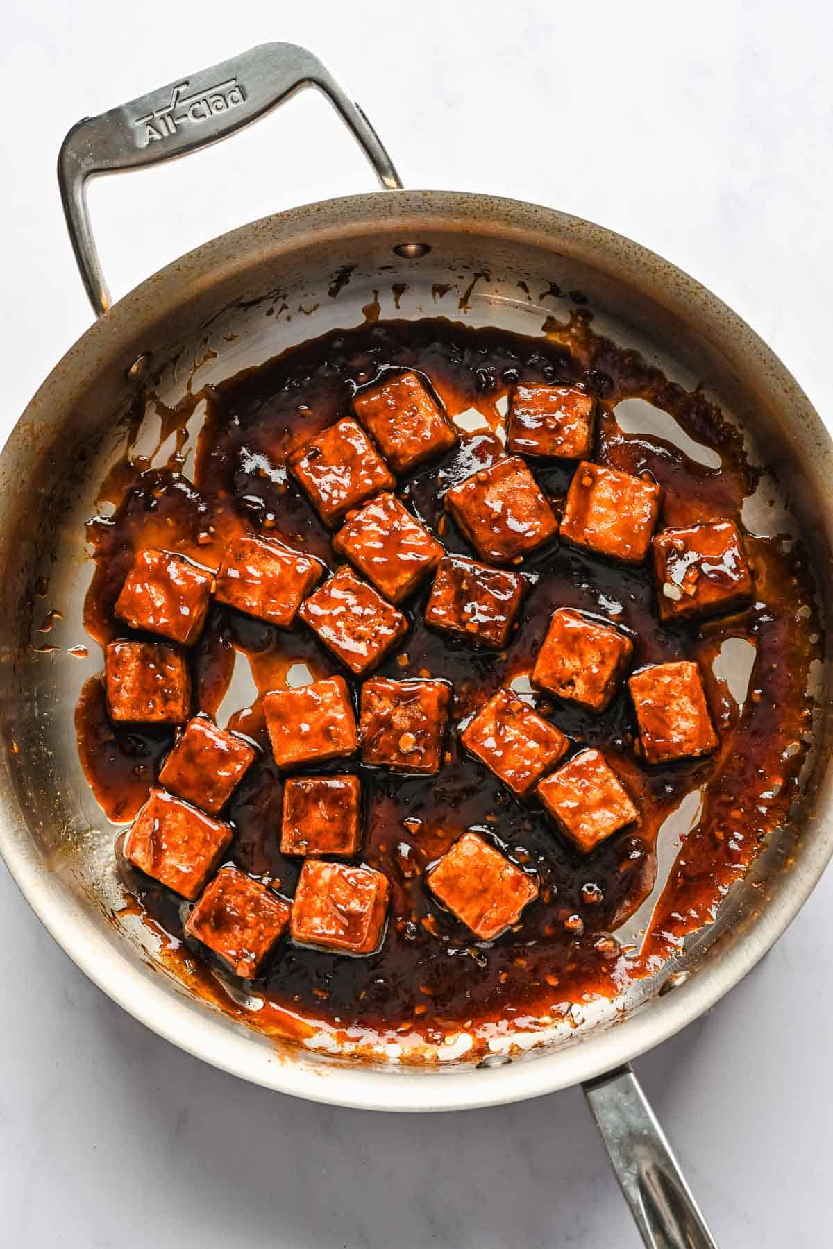 Fried tofu combined with sesame garlic sauce in a metal skillet.