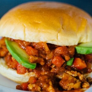 A pumpkin BBQ sloppy joes sandwich garnished with avocado slices, spilling out of the bun on a plate.