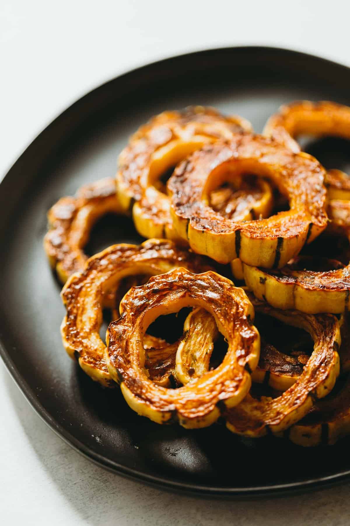 Rings of roasted delicata squash layered on a black plate
