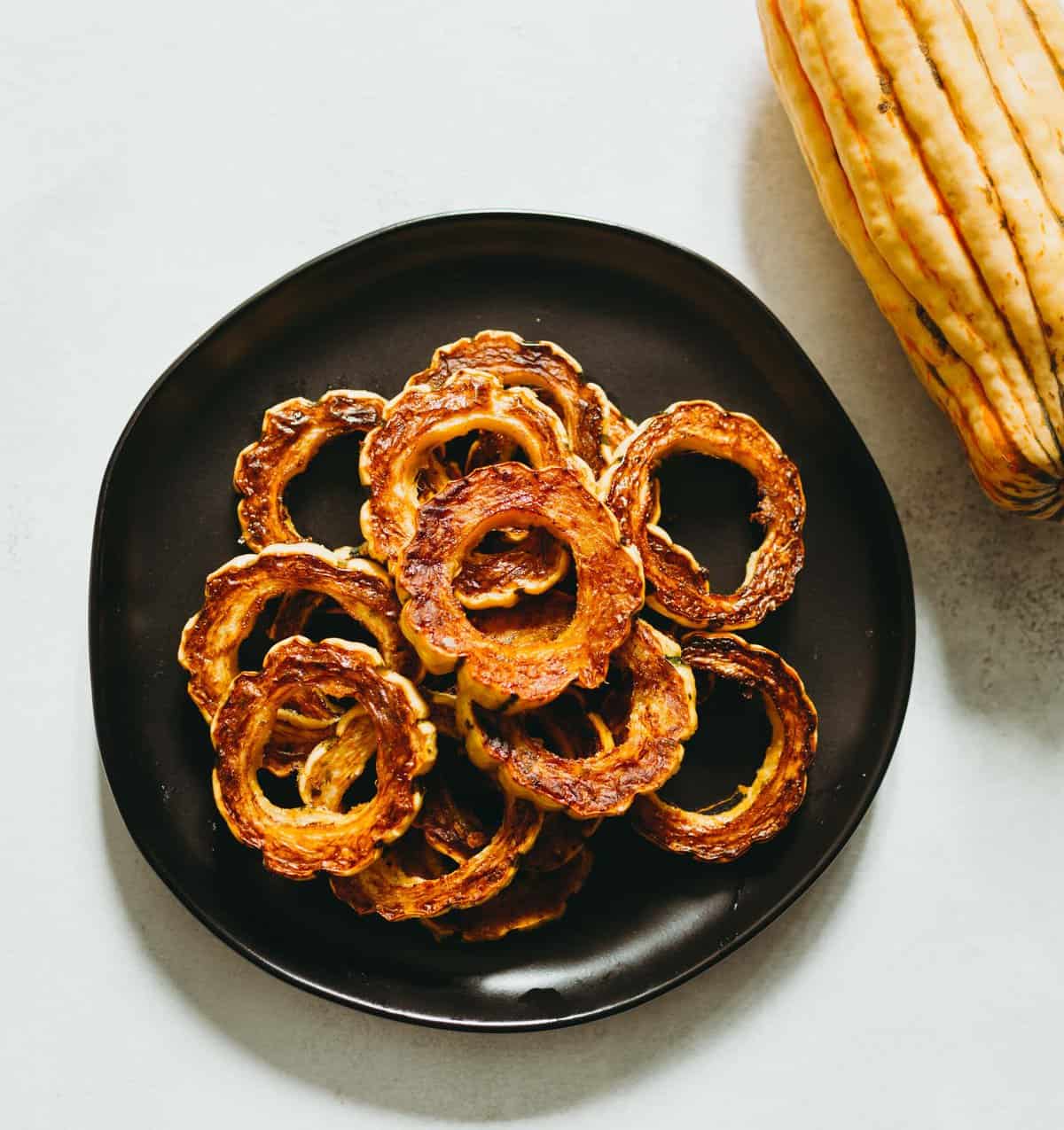 Overhead view of roasted delicata squash rings on black plate