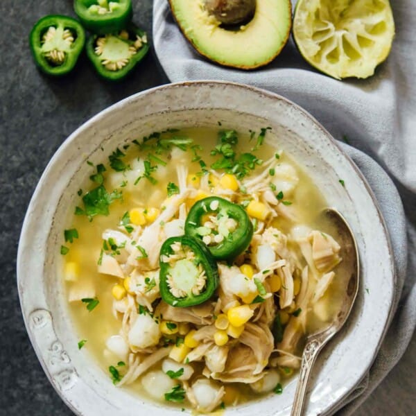Instant Pot jalapeño lime chicken soup in a white bowl with metal spoon next to jalapenos, limes, and avocados